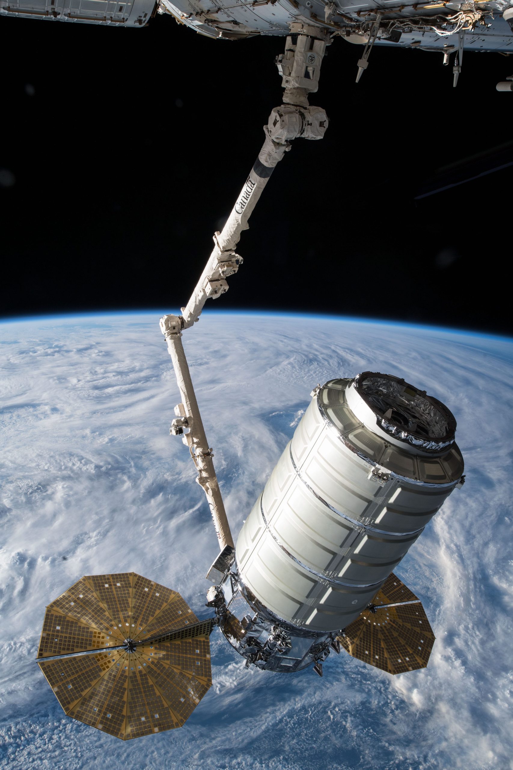 The Orbital ATK space freighter is slowly maneuvered by the Canadarm2 robotic arm scaled