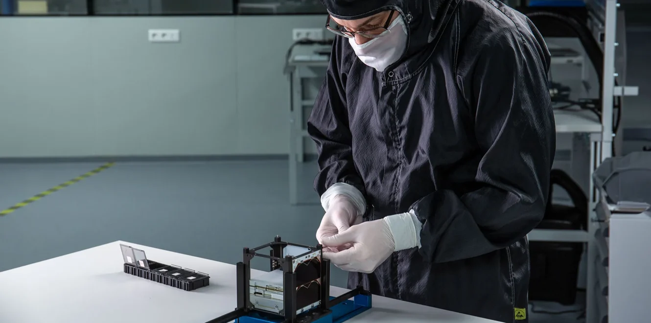 A side view of a EnduroSat technician building a 1U CubeSat satellite bus in a cleanroom production facility.