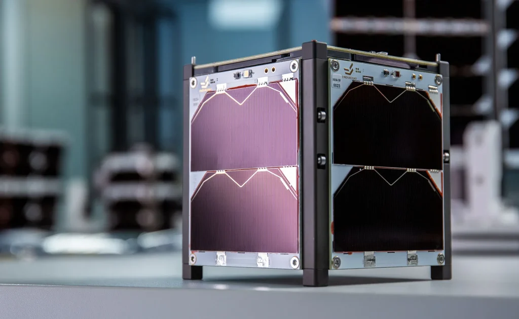 Three quarters side view of the EnduroSat 1U CubeSat satellite bus, pictured in a cleanroom production facility, showing the 1U Solar Panel X/Y and 1U Solar Panel Z mounted on the sides of the nanosatellite.