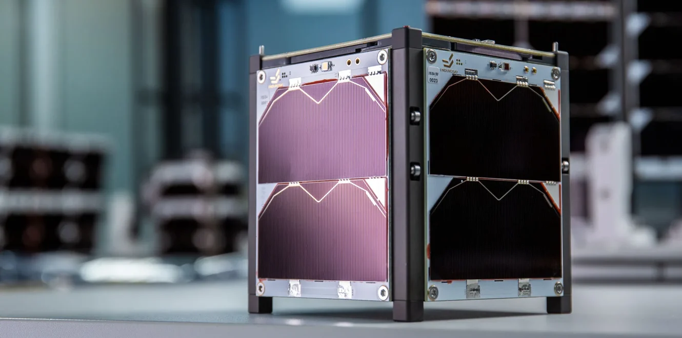 Three quarters side view of the EnduroSat 1U CubeSat satellite bus, pictured in a cleanroom production facility, showing the 1U Solar Panel X/Y and 1U Solar Panel Z mounted on the sides of the nanosatellite.